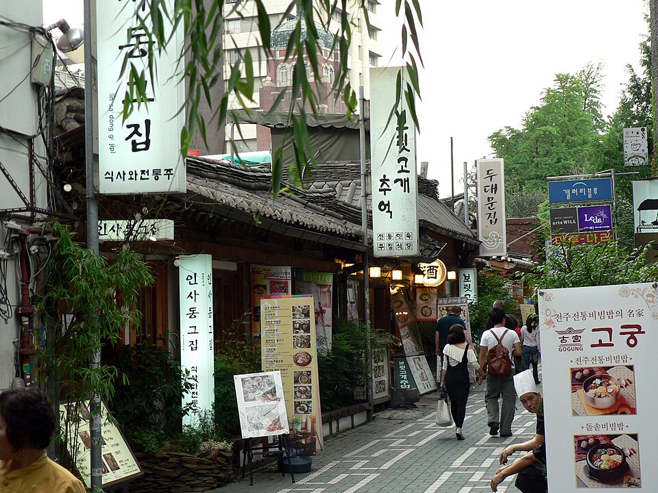 A paved street in Insadong with tiled-roof restaurant fronts, vertical signs and people walking