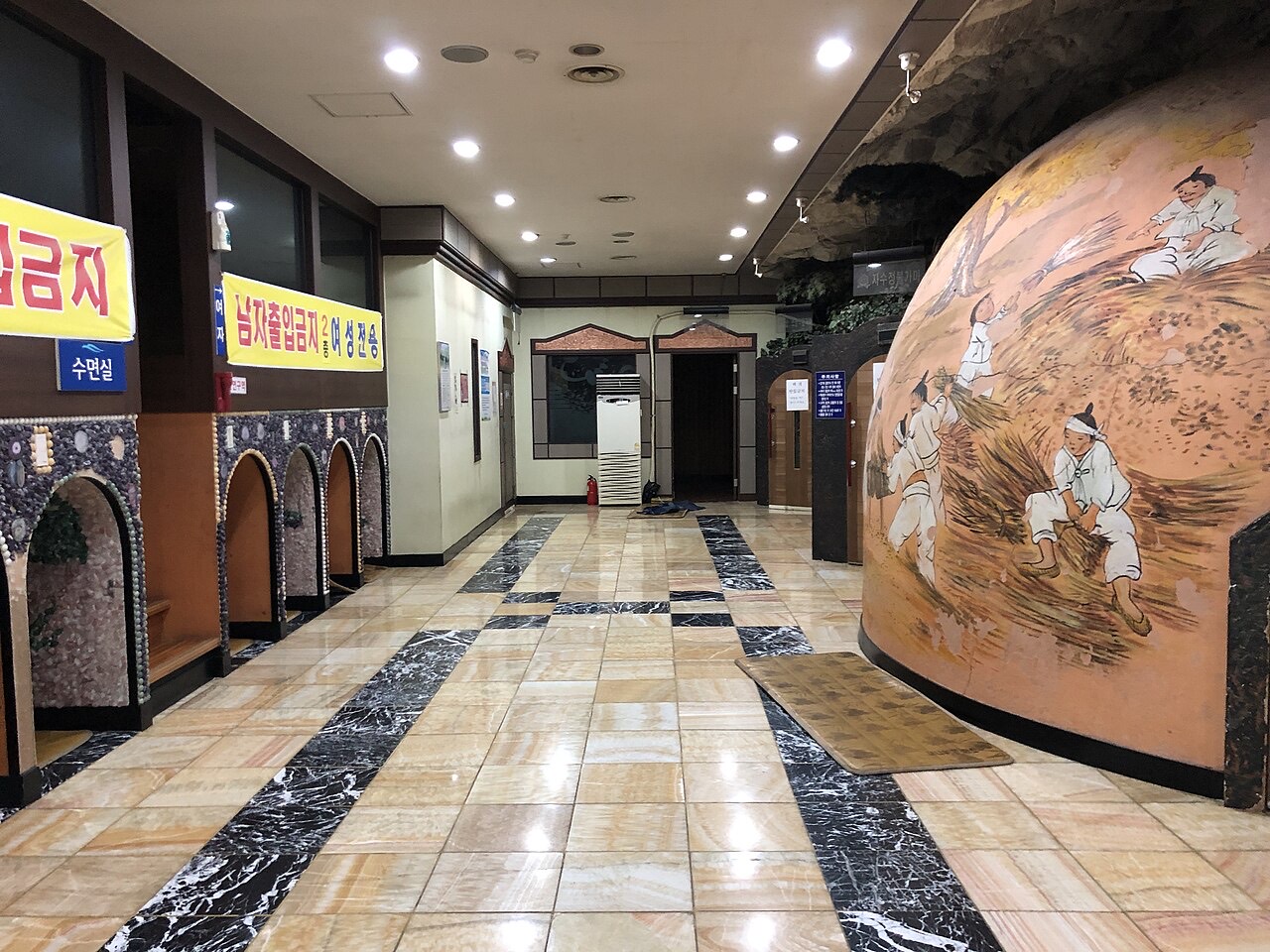 A tiled hall in a jjimjilbang with a large dome painted with a farming scene on the right and arched stone doorways on the left