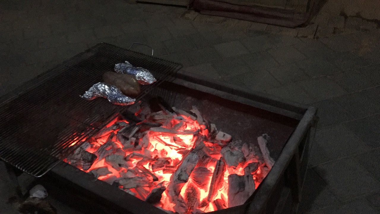 Sweet potatoes wrapped in foil on a grill over glowing red charcoal
