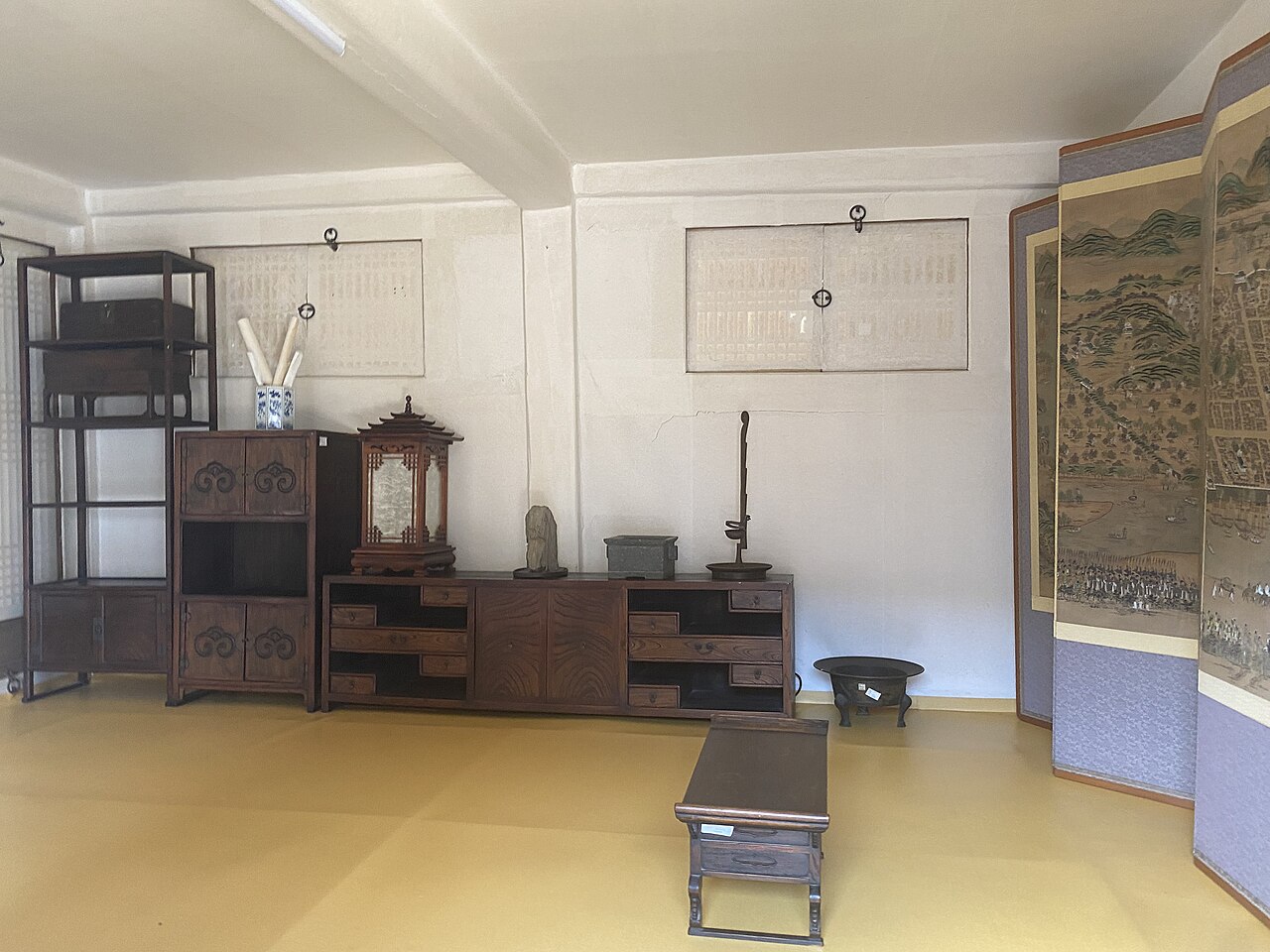 Inside a hanok at Namsangol Hanok Village: wooden cabinets and a lantern along a white wall, a folding screen on the right and a paper-covered floor